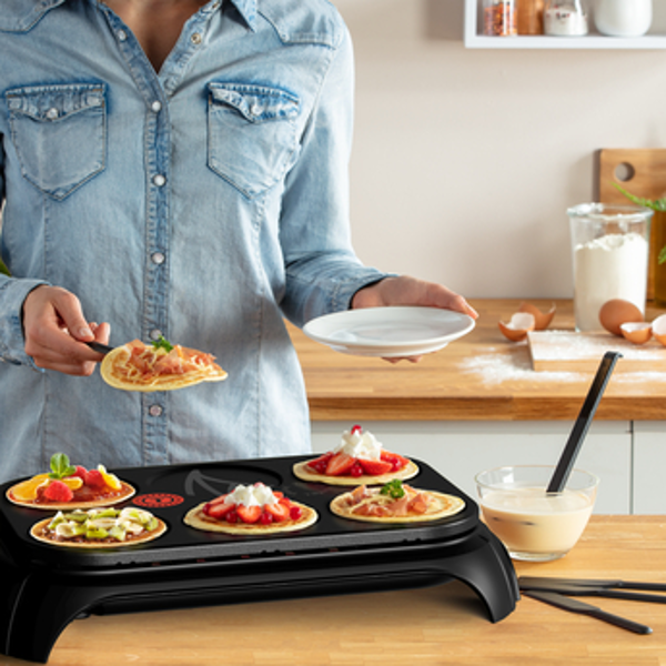 Une personne avec des crêpes et des garnitures. Une poêle avec des crêpes et des garnitures est sur le poêle.