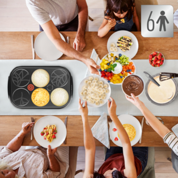 Vue aérienne d'un repas de famille. Crêpes, fruits et garnitures sont étalés sur la table.
