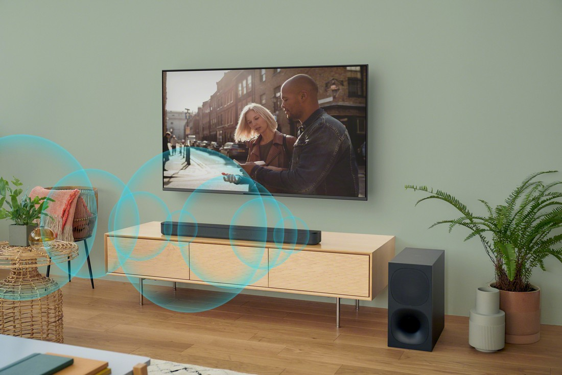 TV con pareja. Barra de sonido y subwoofer al frente. Ondas de sonido azules emanan de la barra.