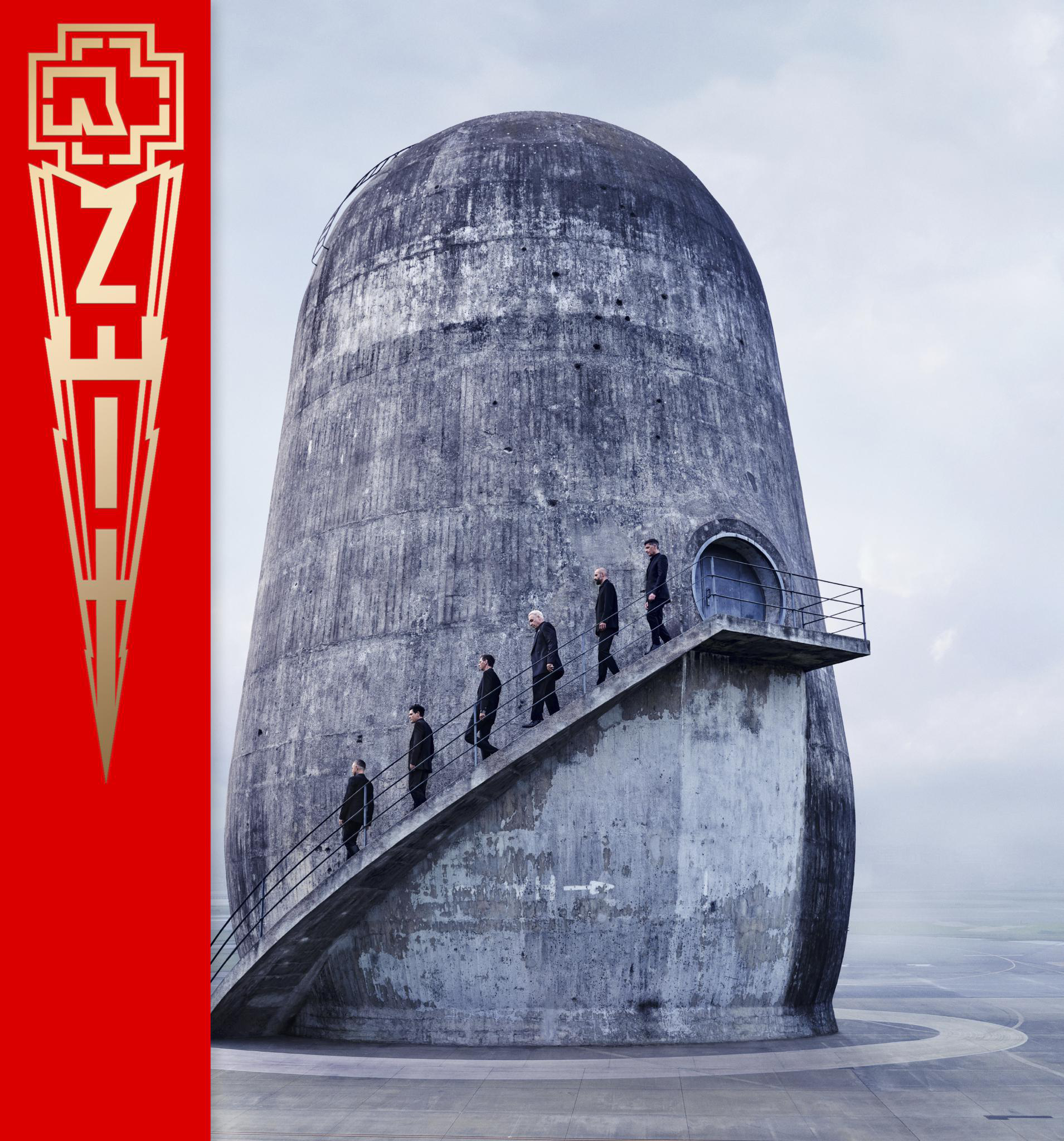 Bandmitglieder gehen die Treppe eines betonartigen Silos hinauf. Rotes Banner links.
