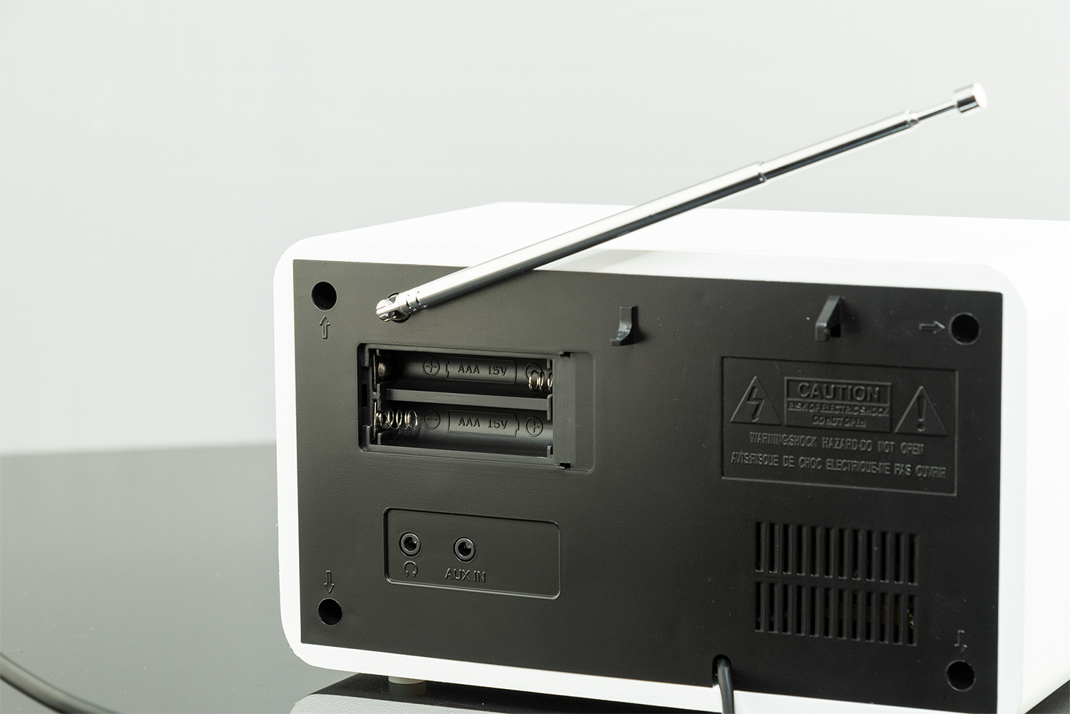 Achterkant van een witte radio met zwart paneel, antenne en batterijvak.