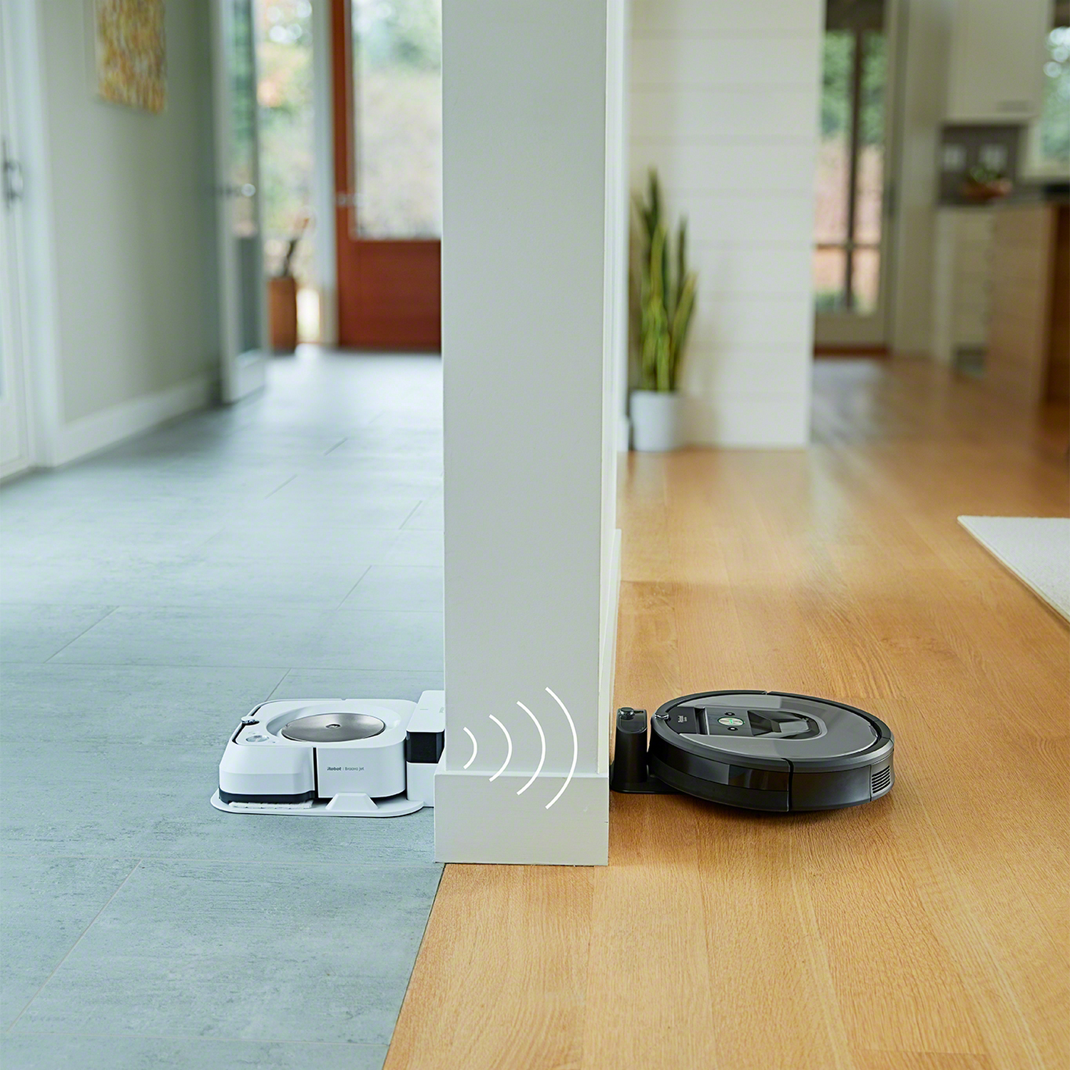 Aspiradora robot cerca de una pared y una fregona en un suelo de madera en un entorno doméstico.