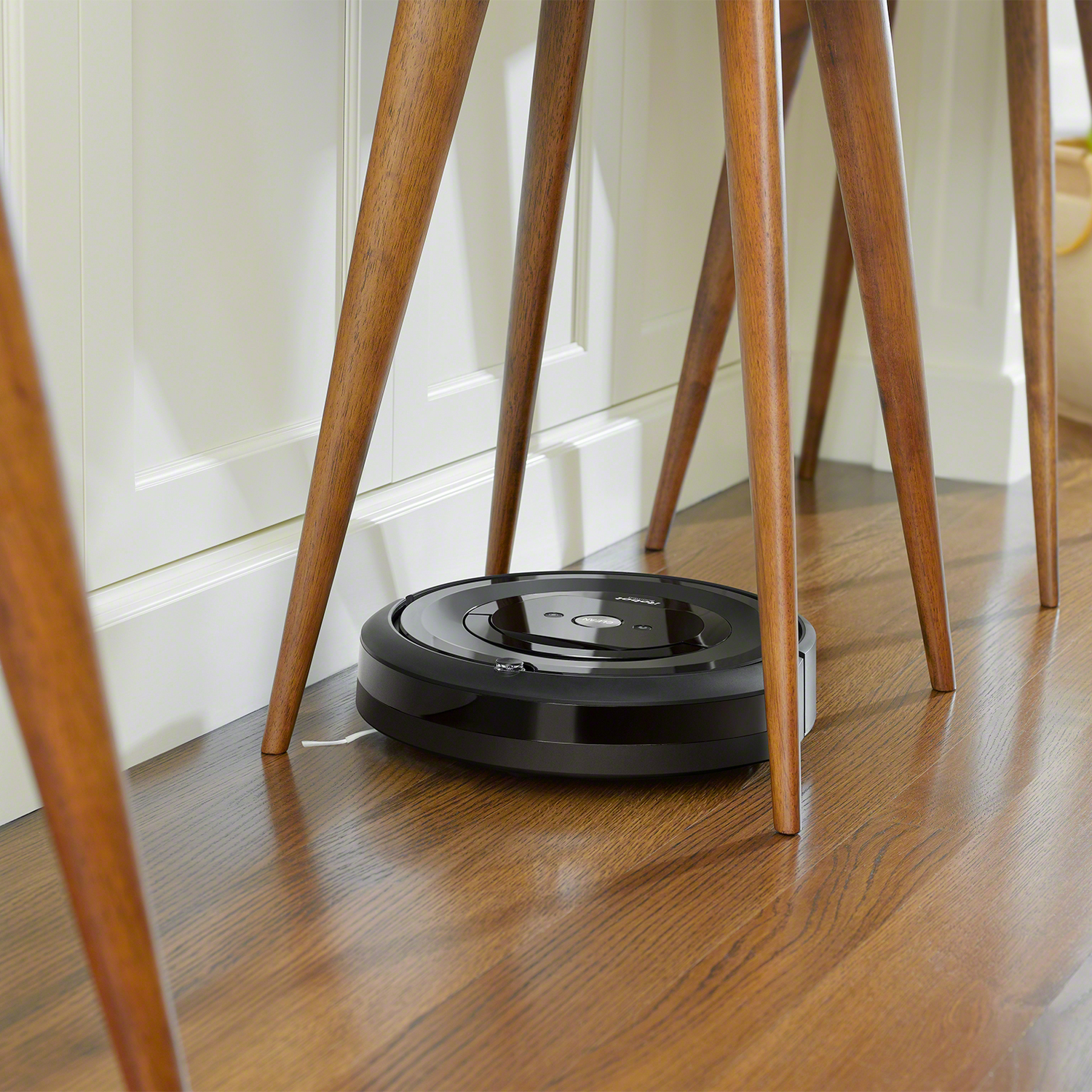 Aspiradora robot limpiando bajo patas de mesa de madera en suelo de madera.