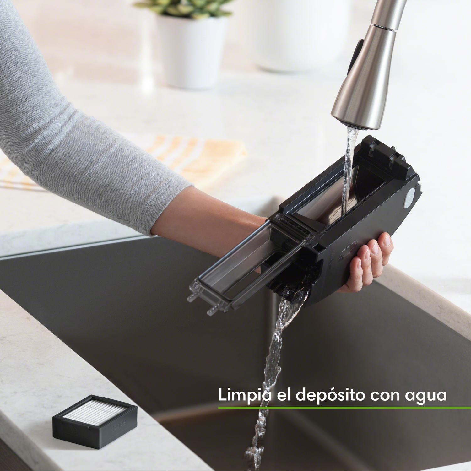 La mano de una persona enjuagando un componente de limpieza negro bajo un grifo plateado.