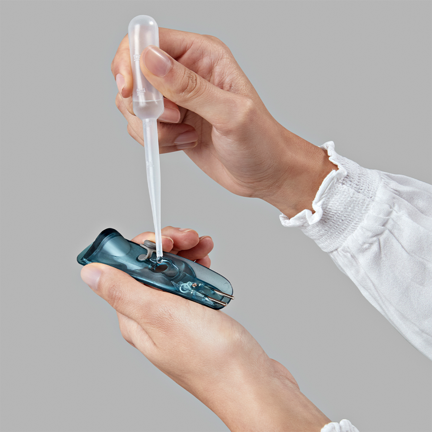 Mani usano una pipetta per riempire un contenitore di plastica blu.
