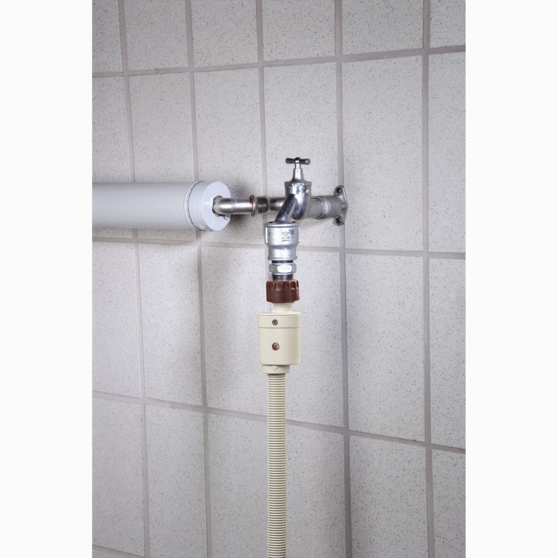 Ein Wasserhahn, der an einen Schlauch angeschlossen ist. Der Schlauch ist beige und mit einer weißen Wand verbunden.