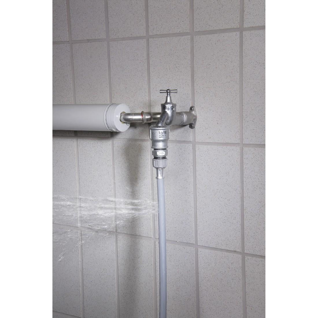 Wasserhahn, Schlauch und Rohr an einer gefliesten Wand.