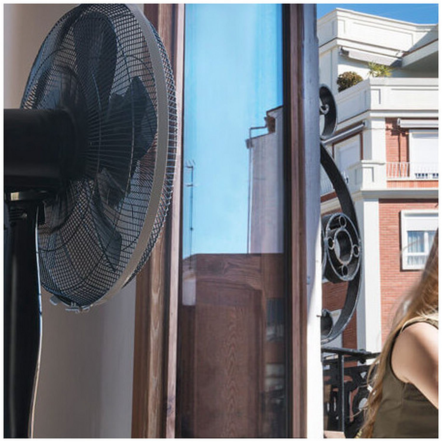 Un ventilador negro y una ventana que muestra un edificio con balcón.