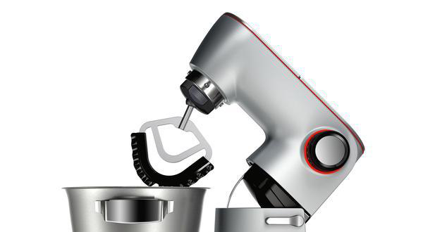 Silberfarbener Küchenmixer mit roten Akzenten und Aufsätzen über einer silbernen Schüssel, vor weißem Hintergrund.