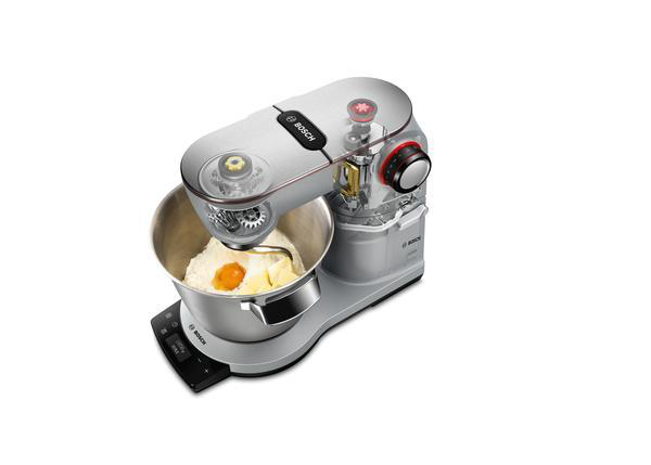 Ein silberfarbener Küchenmixer mit einer Schüssel mit Zutaten. Oben ein roter Knopf.