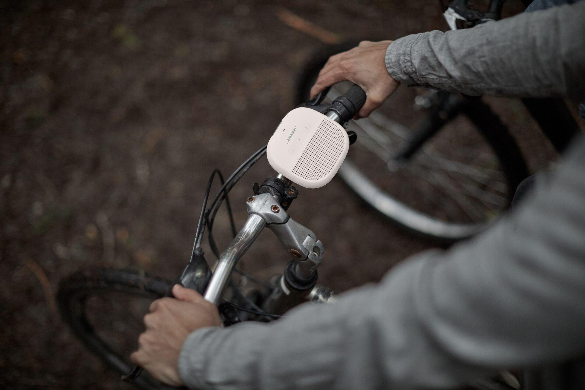 Eine Person hält einen weißen Bose-Lautsprecher auf einem Fahrrad.