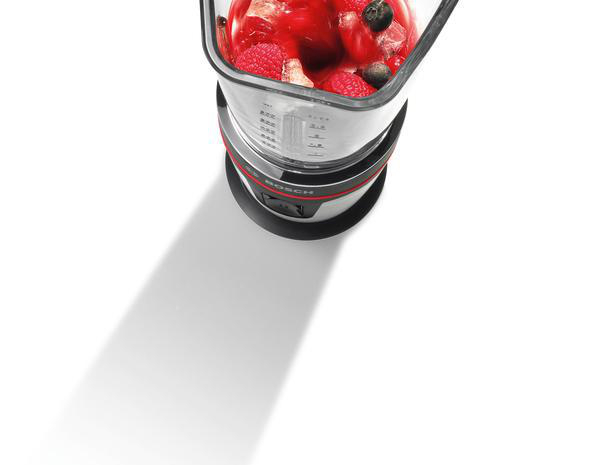 Ein Mixer mit rotem und schwarzem Sockel ist mit Beeren und Eis gefüllt, weißer Hintergrund.