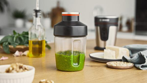 Ein Mixer mit Pesto und Zutaten auf einem Holztisch.