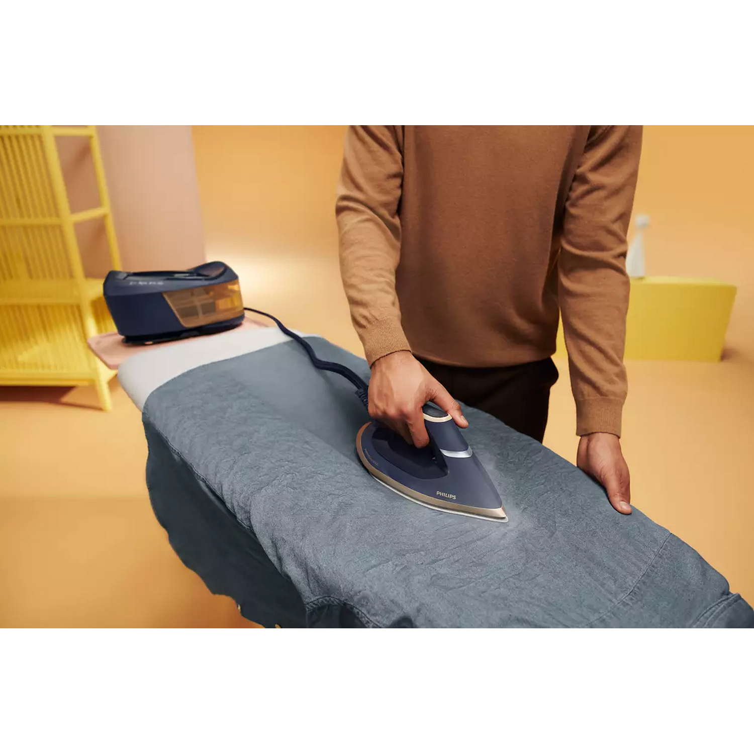 Persona planchando una camisa azul en una tabla de planchar, con un depósito de agua al lado.