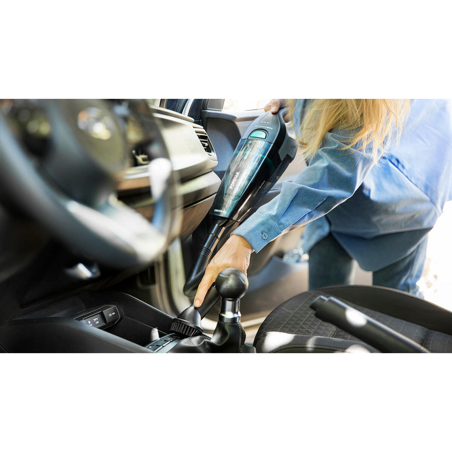 Mujer usando una aspiradora de mano en un coche.