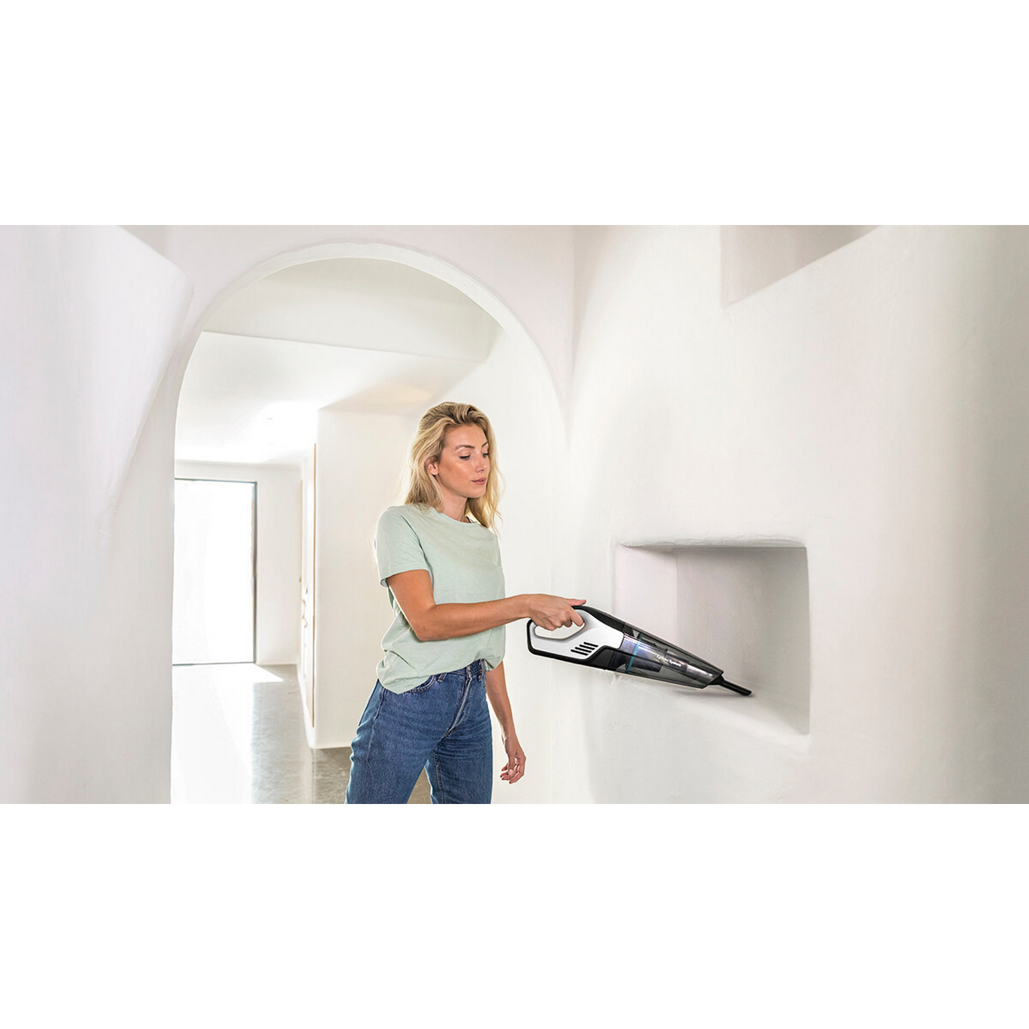 Mujer aspirando una pared blanca con una aspiradora de mano en un arco.