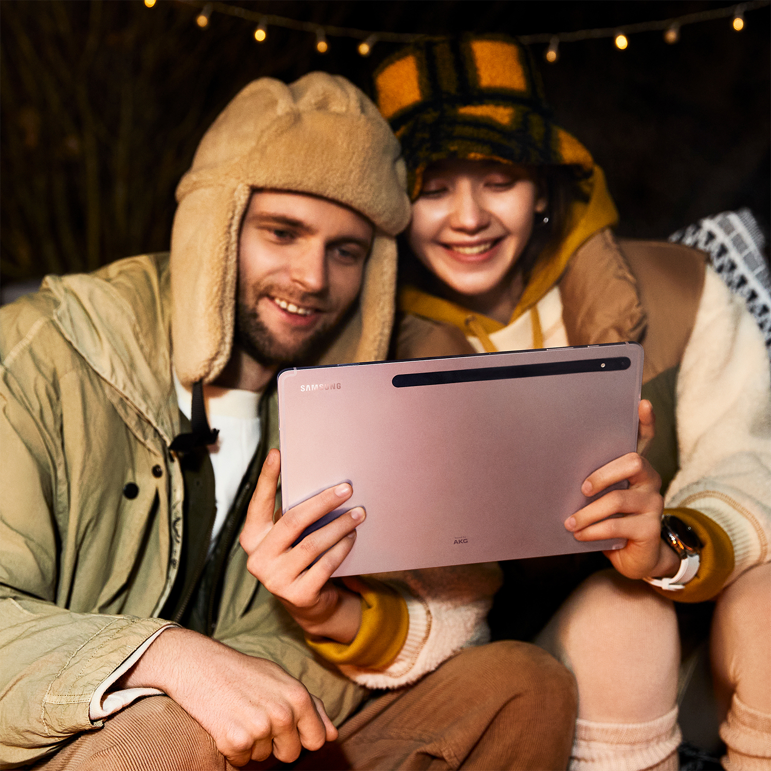 Dos personas mirando una tableta, al aire libre por la noche con iluminación suave.