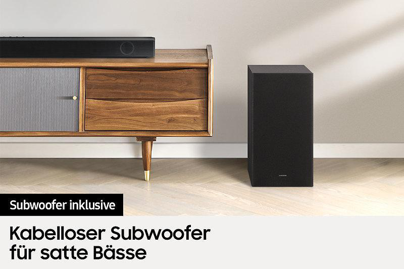 Eine schwarze Soundbar und ein schwarzer Subwoofer auf einem Holzschrank. Deutscher Text über Sound.