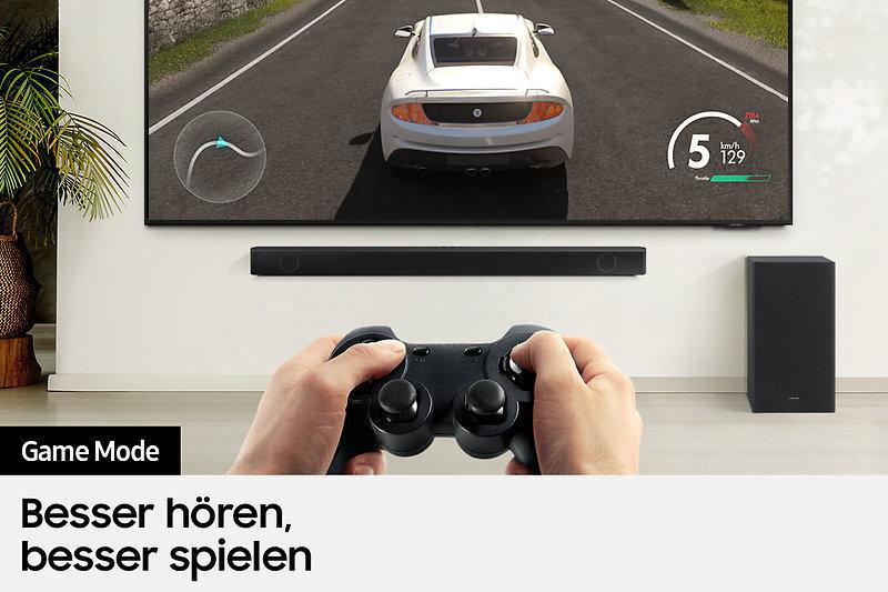 Eine Person, die einen Gamecontroller vor einem Fernseher hält, mit einer Soundbar darunter.