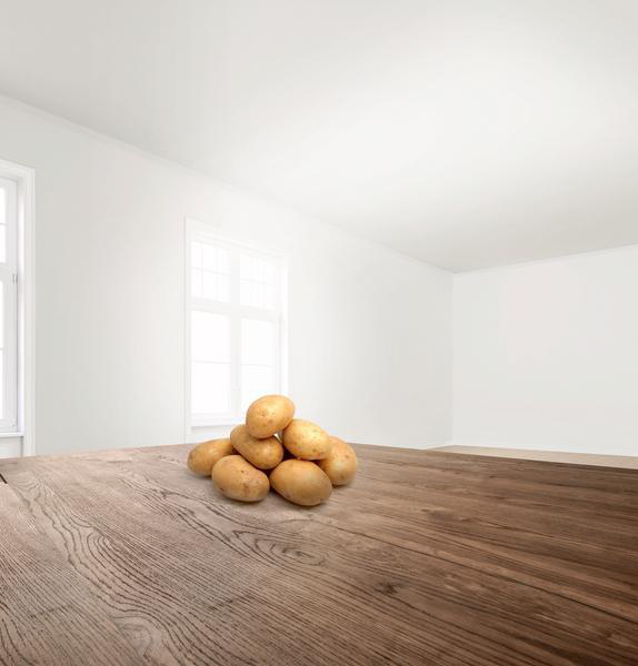 Ein Haufen Kartoffeln auf einem Holztisch. Leere weiße Wände und Decke im Hintergrund.