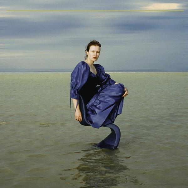 Frau in blauem Kleid sitzt auf transparentem Stuhl im Wasser, mit bewölktem Himmel.