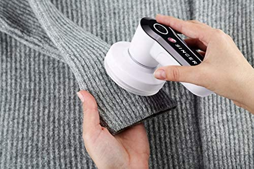 Une personne utilisant un destructeur de peluches sur un tissu gris, tenant le tissu et l'outil.