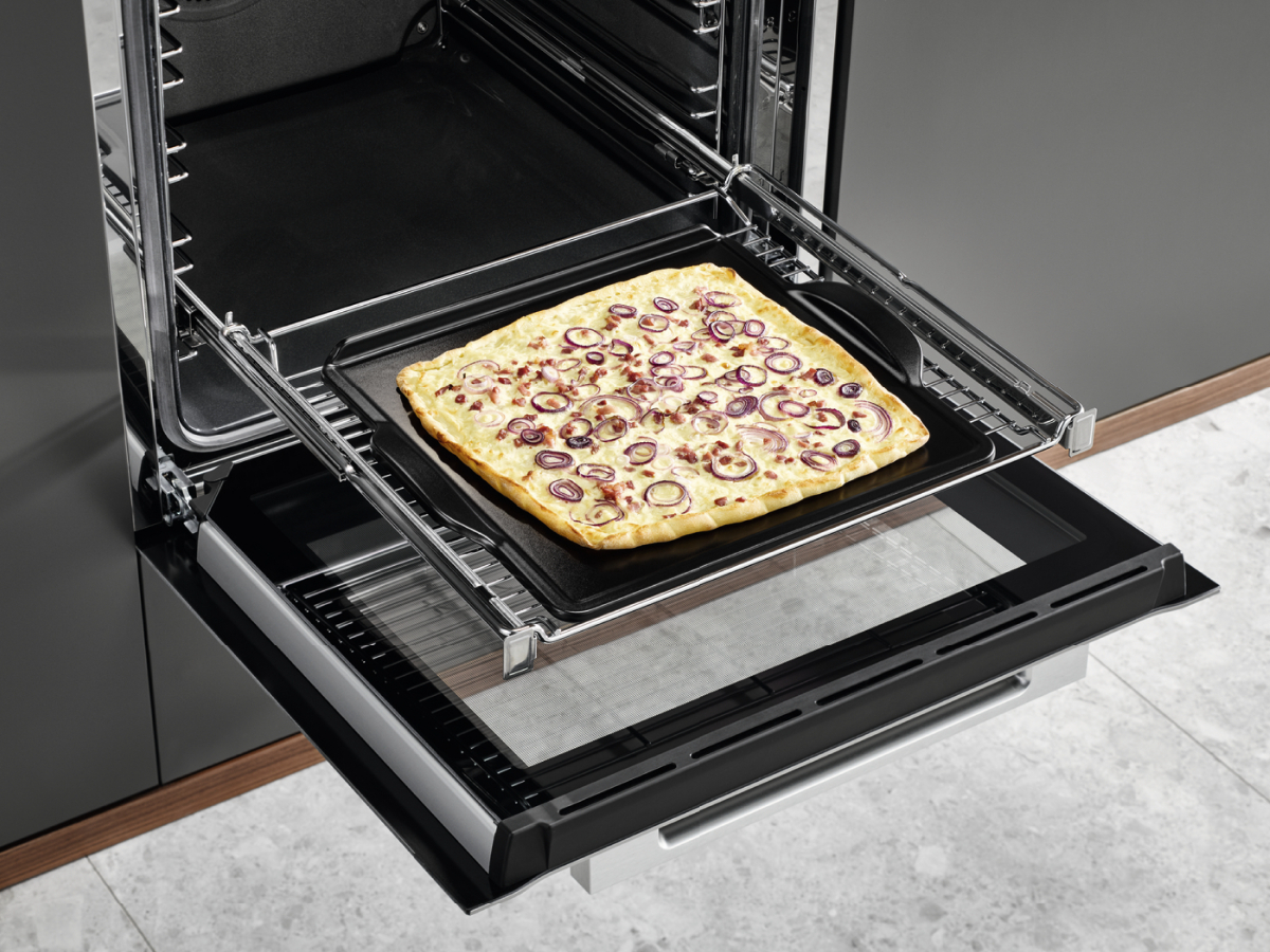 Nyitott sütő pizzával egy tálcán, vöröshagymával. Fekete sütő és sötét háttér.