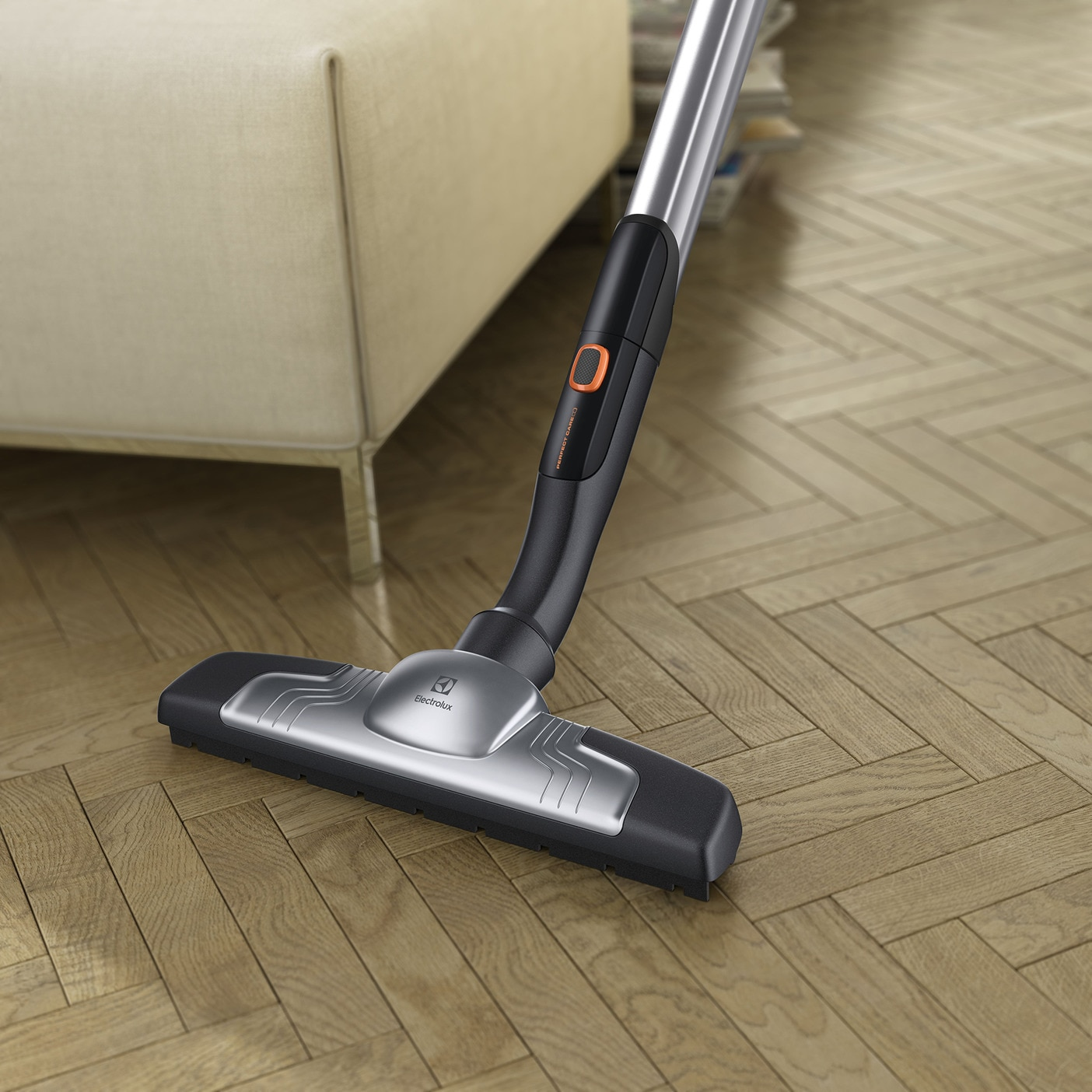 Tête d'aspirateur sur un sol en bois. La tête est argentée et noire. L'arrière-plan est un canapé beige.
