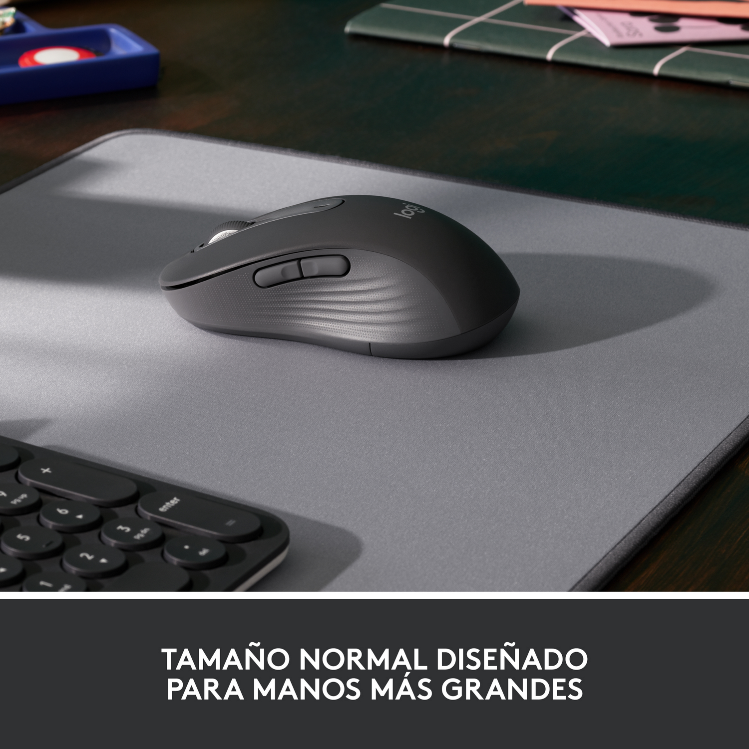 Un ratón inalámbrico negro sobre una alfombrilla gris, con un teclado en el fondo.