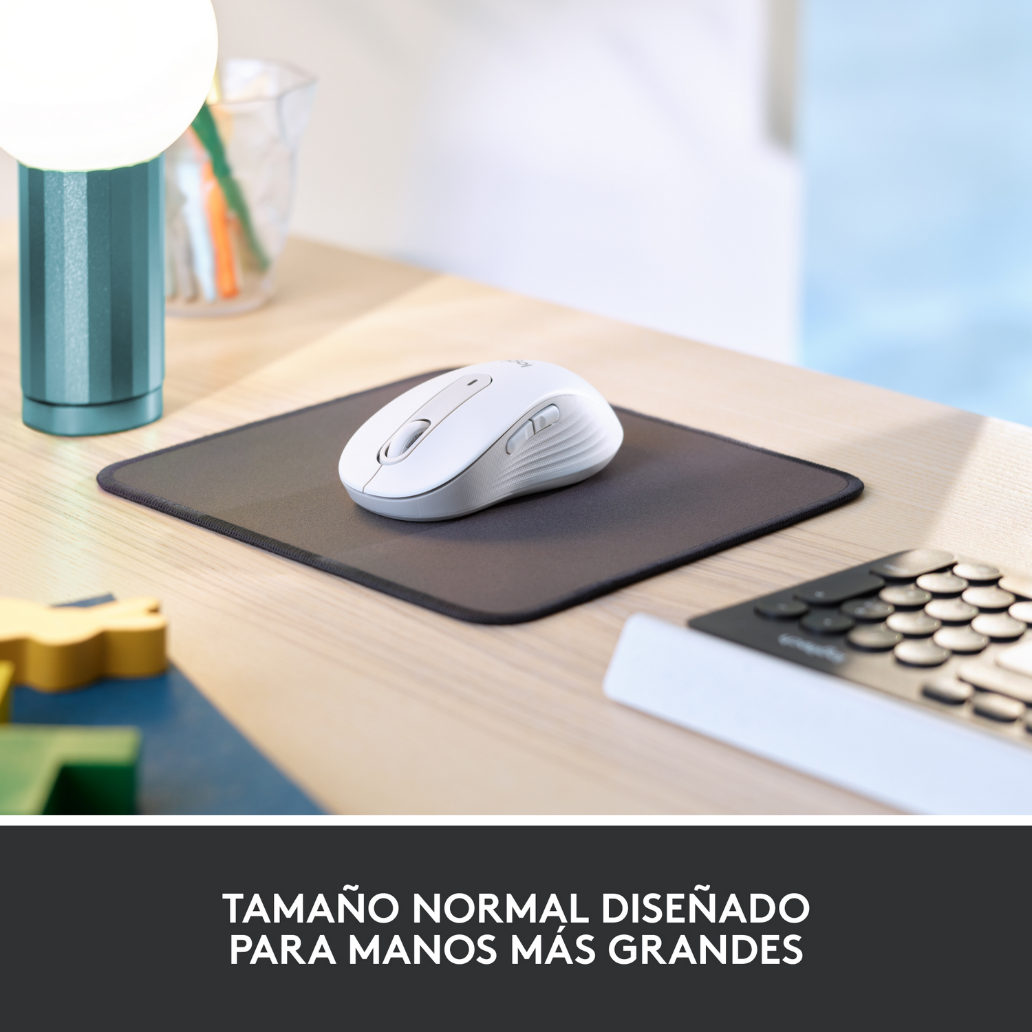 Un ratón blanco sobre una alfombrilla negra. Una lámpara y un teclado en el fondo. Texto en español abajo.