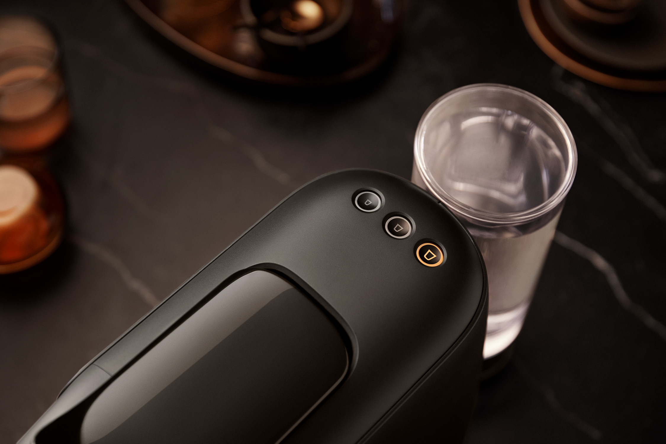 Coffee machine with three buttons and a glass of water next to it.