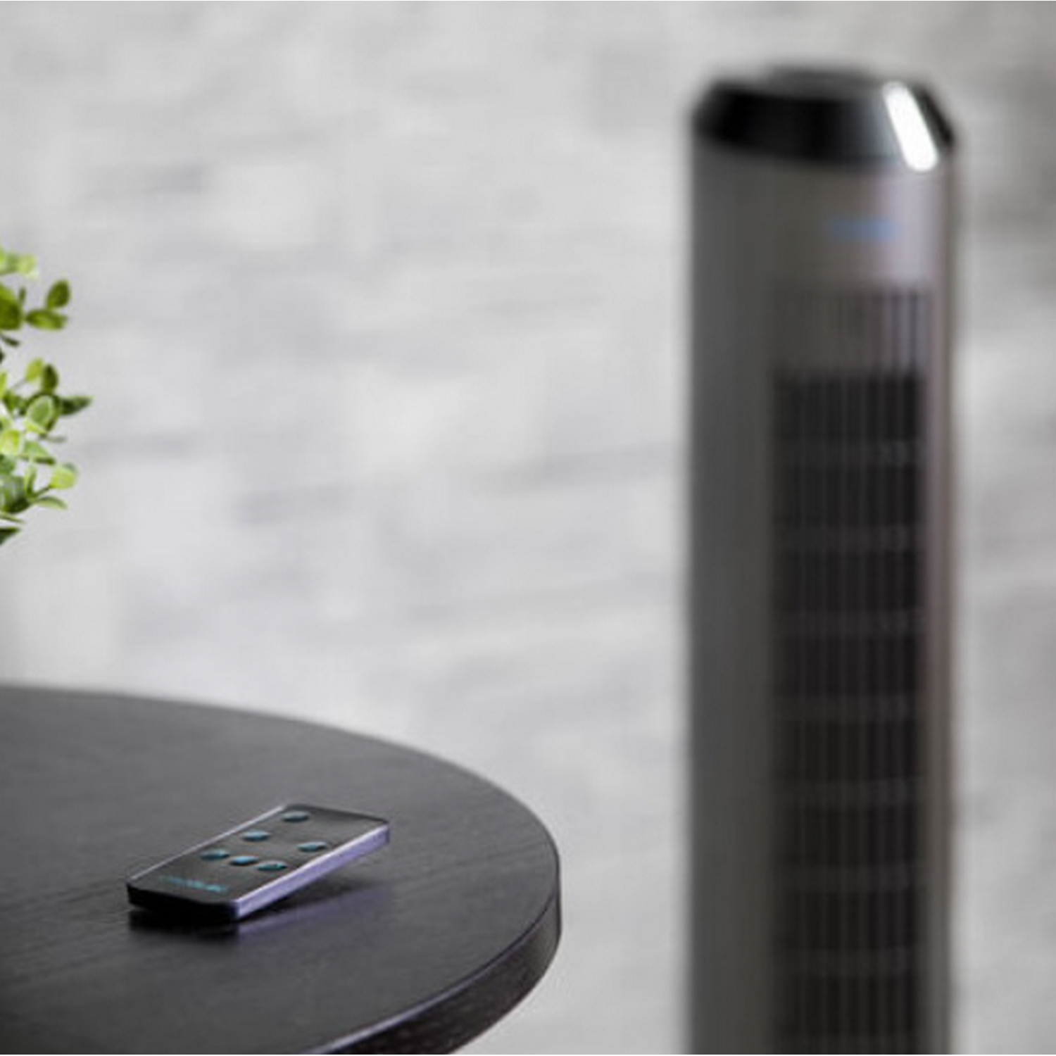 Ventilador alto y mando a distancia en una mesa. El fondo es una pared de ladrillo.