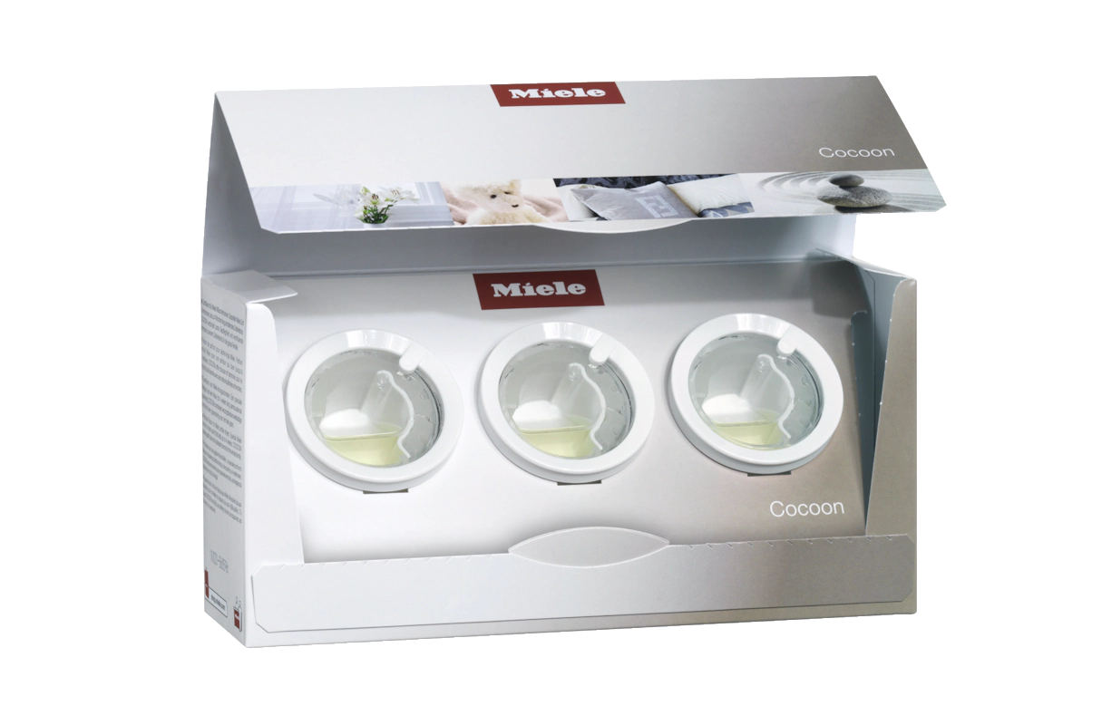 Eine weiße Box mit drei Fächern, die jeweils eine Reinigungskapsel enthalten. Das Miele-Logo ist sichtbar.