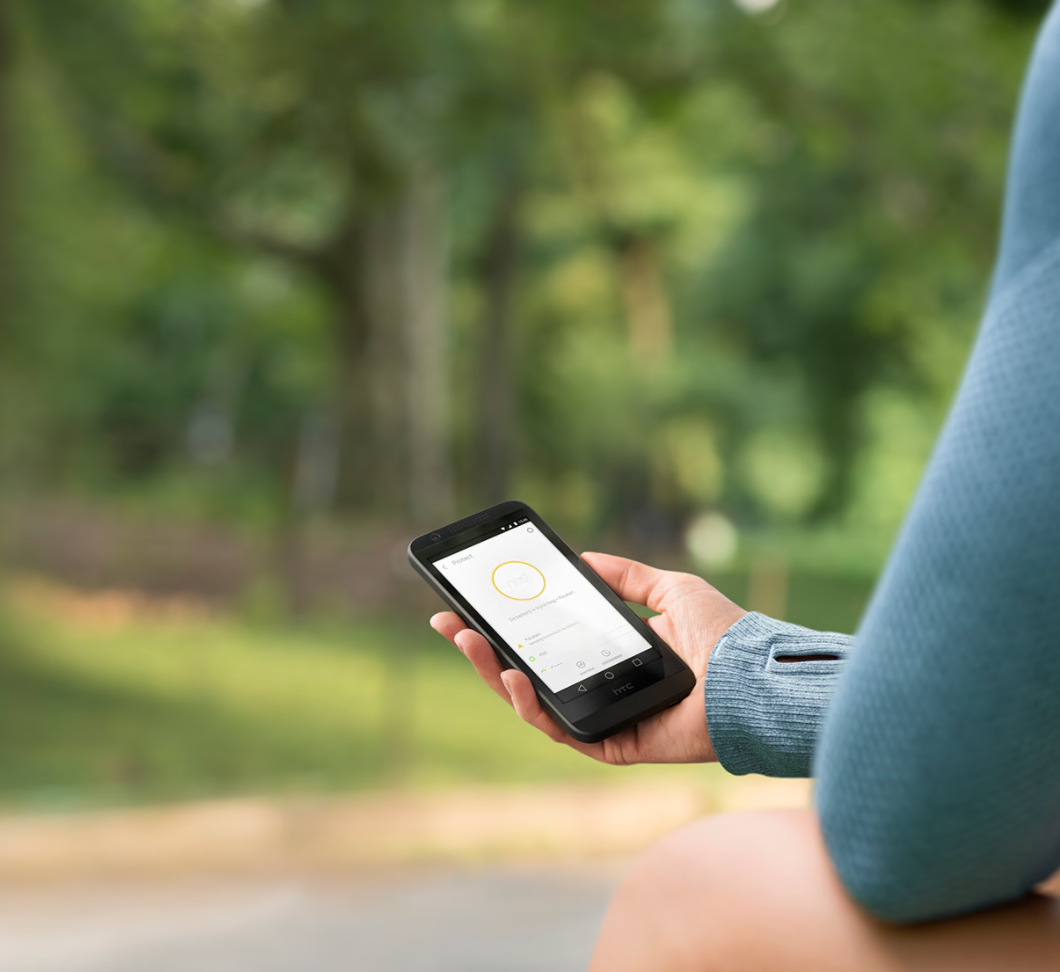 Een hand houdt een zwarte HTC-telefoon vast, met een app. Groene bomen zijn wazig op de achtergrond.