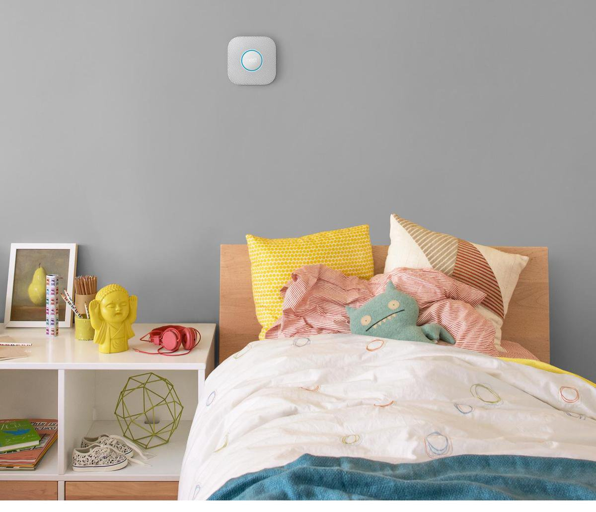 Nest rookmelder aan een muur boven een bed. Er zijn speelgoed en kussens.