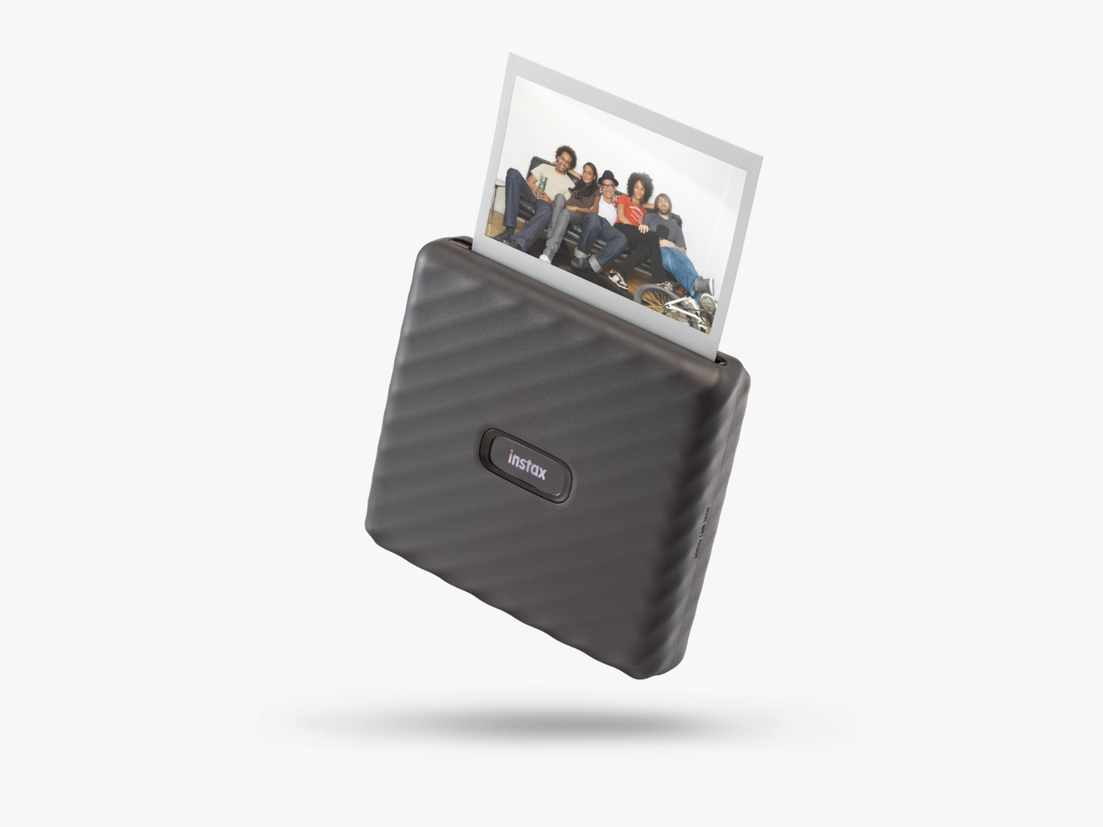 Siyah bir Instax yazıcı bir fotoğraf çıkarıyor. Fotoğraf, bir kanepede oturan bir grup insanı gösteriyor.