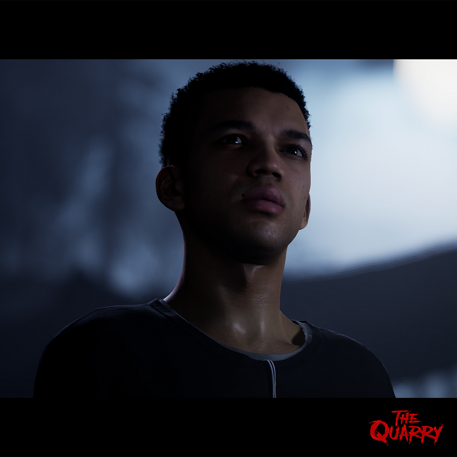 Un hombre con pelo corto y rizado mirando hacia arriba. El fondo es oscuro y borroso. El logo de Quarry está abajo.