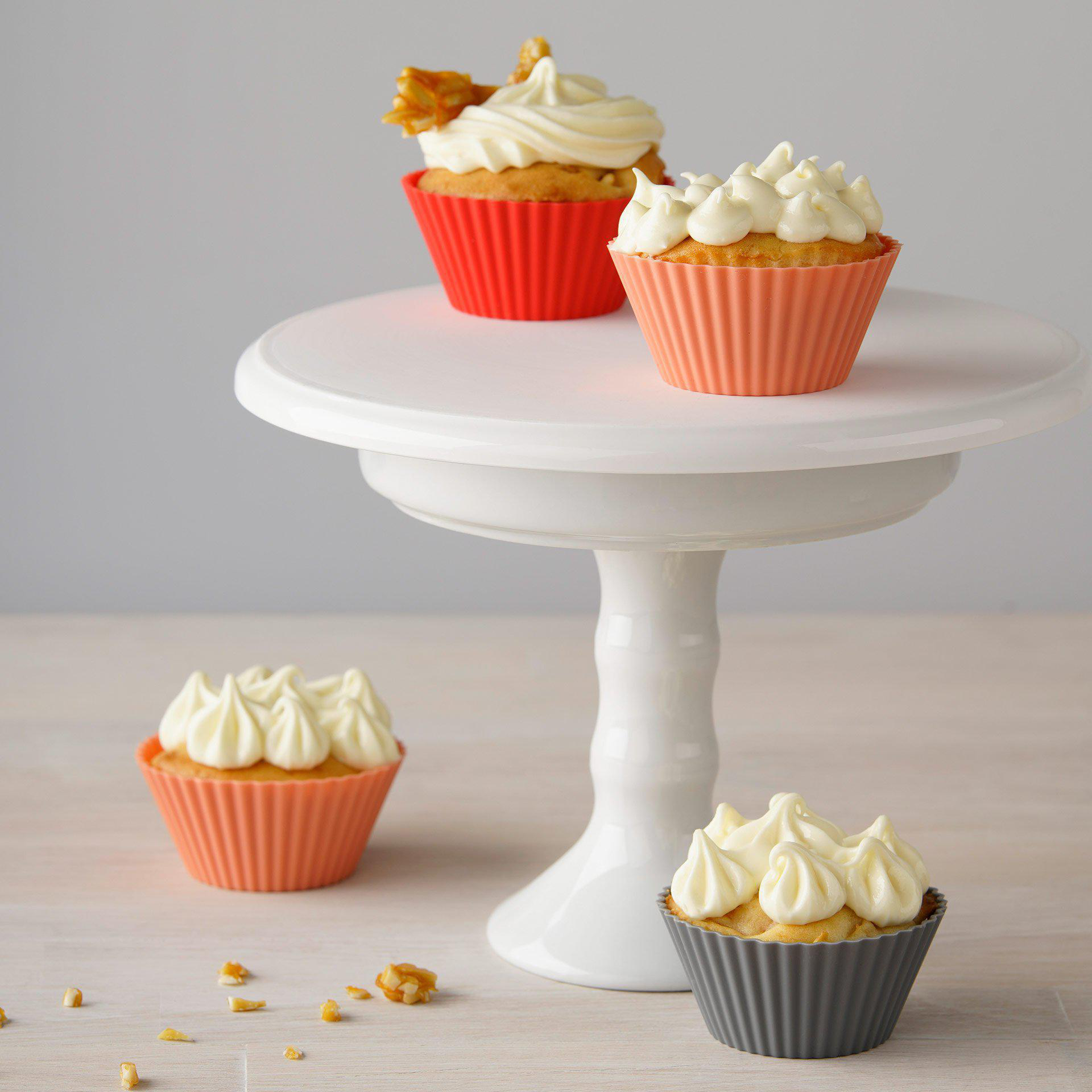Drei Cupcakes auf einem weißen Kuchenständer. Jeder Cupcake hat weißes Frosting und eine andere Farbe.