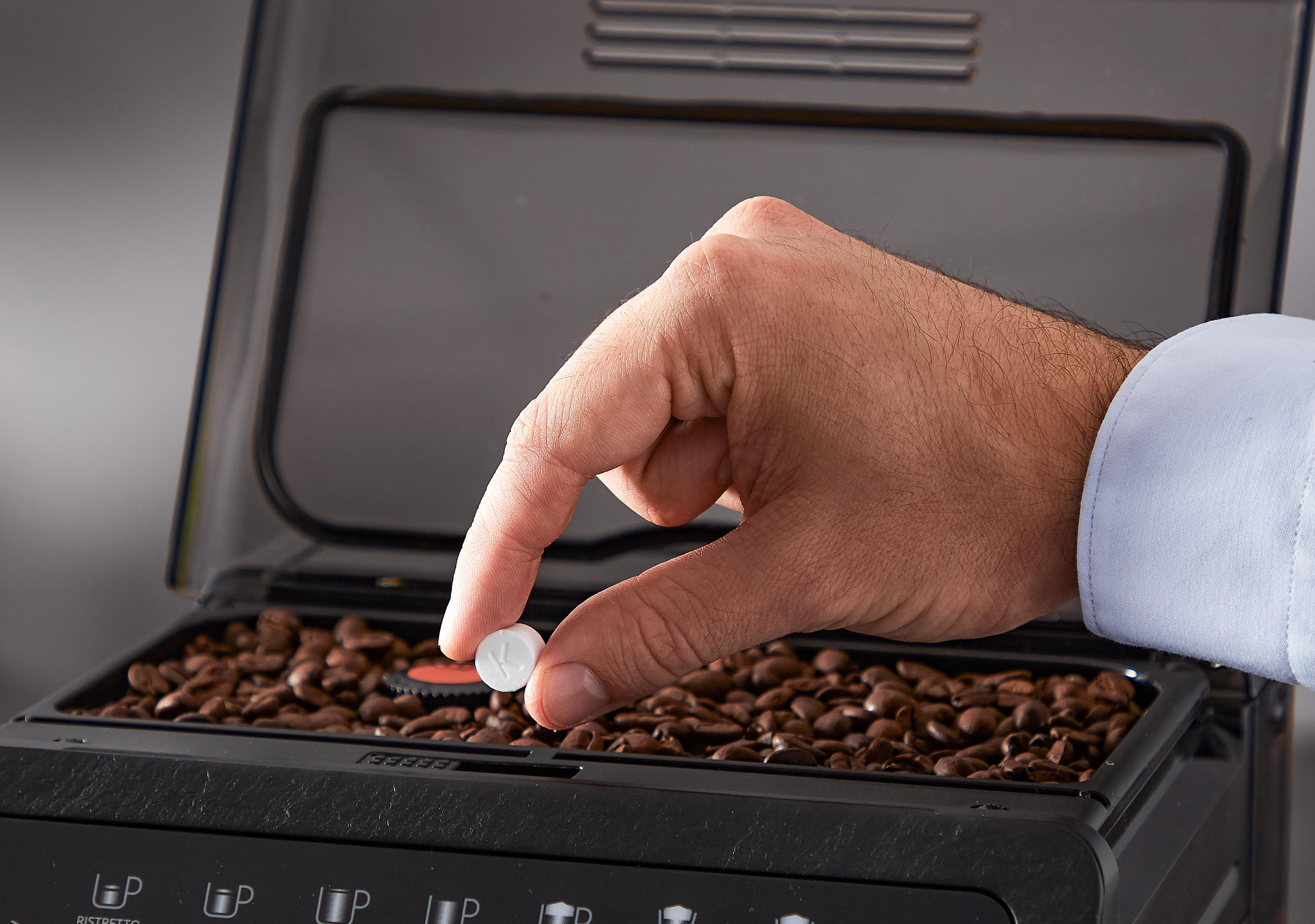 Eine Hand legt Pillen in eine Kaffeemaschine.