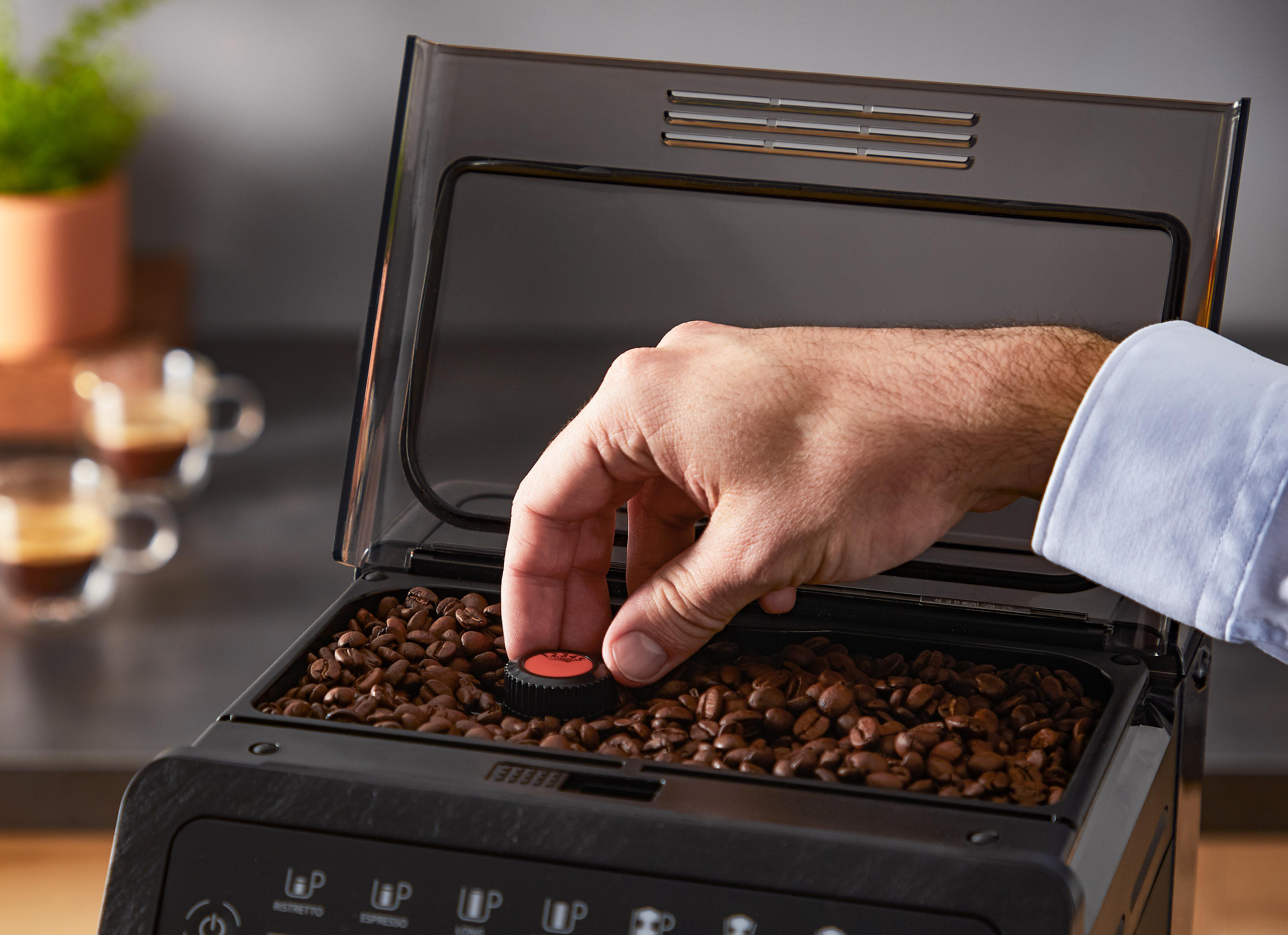 Die Hand einer Person, die Kaffeebohnen in den Bohnenbehälter einer Kaffeemaschine gibt.