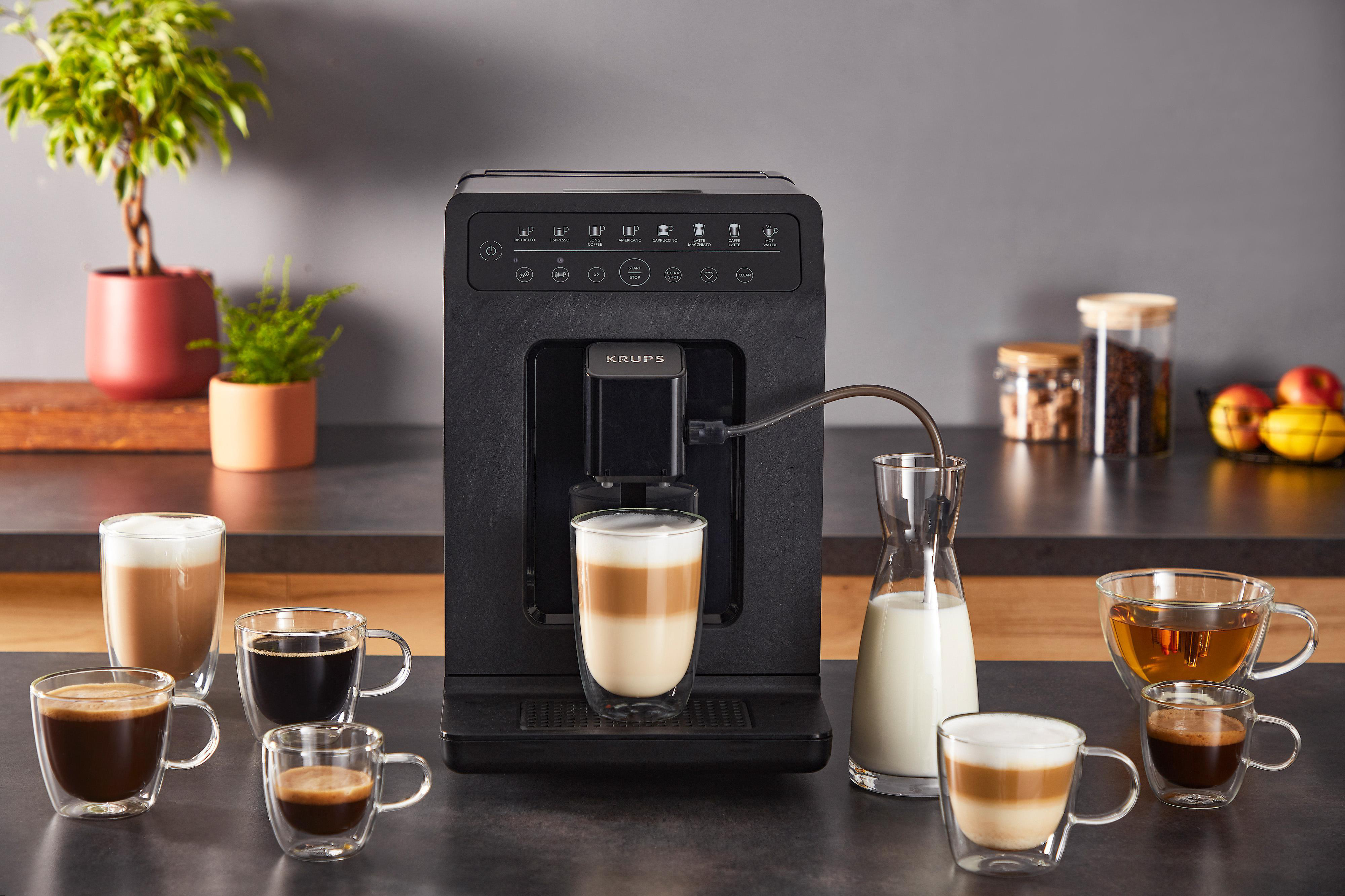 Schwarze Krups Kaffeemaschine mit verschiedenen Kaffeetassen und Milchkanne.