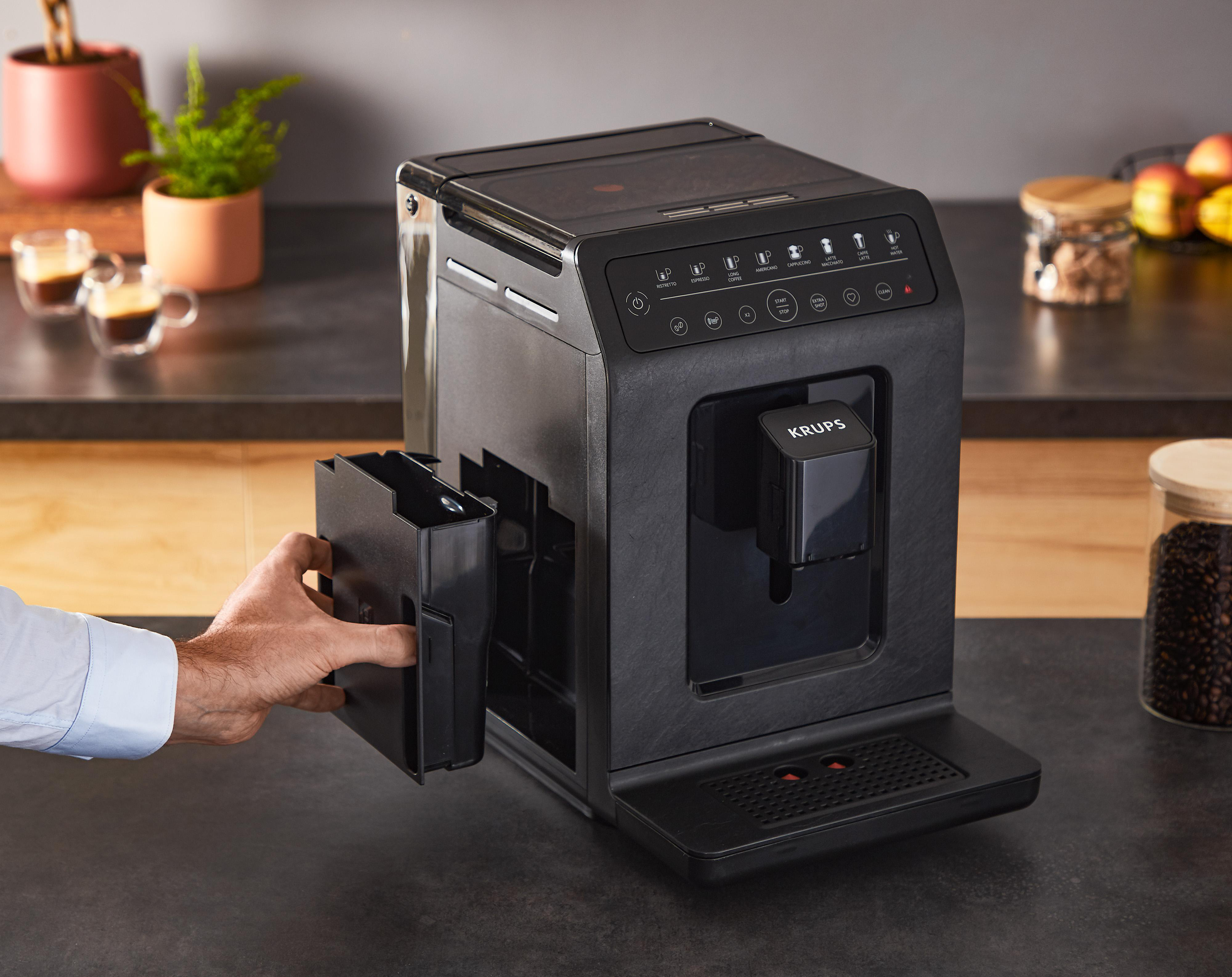 Eine schwarze Kaffeemaschine mit einer Hand, die einen schwarzen Behälter für Kaffeesatz einsetzt.