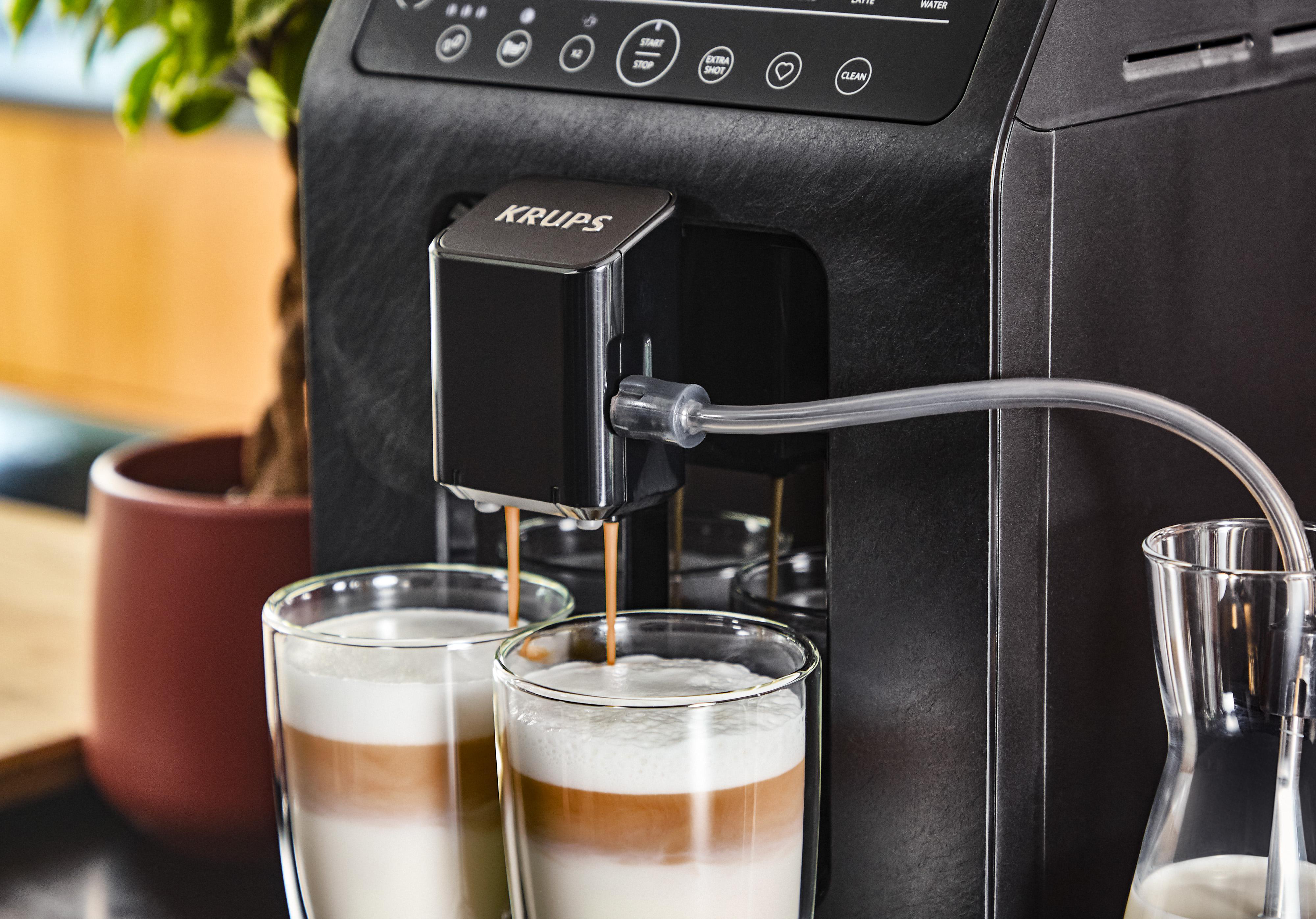 Schwarze Krups Kaffeemaschine, die Kaffee in zwei Gläser ausgibt, mit Milch im Hintergrund.