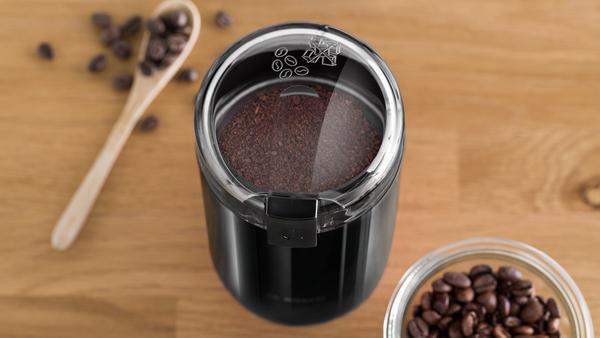 Eine Kaffeemühle mit Kaffeebohnen und gemahlenem Kaffee, Draufsicht.