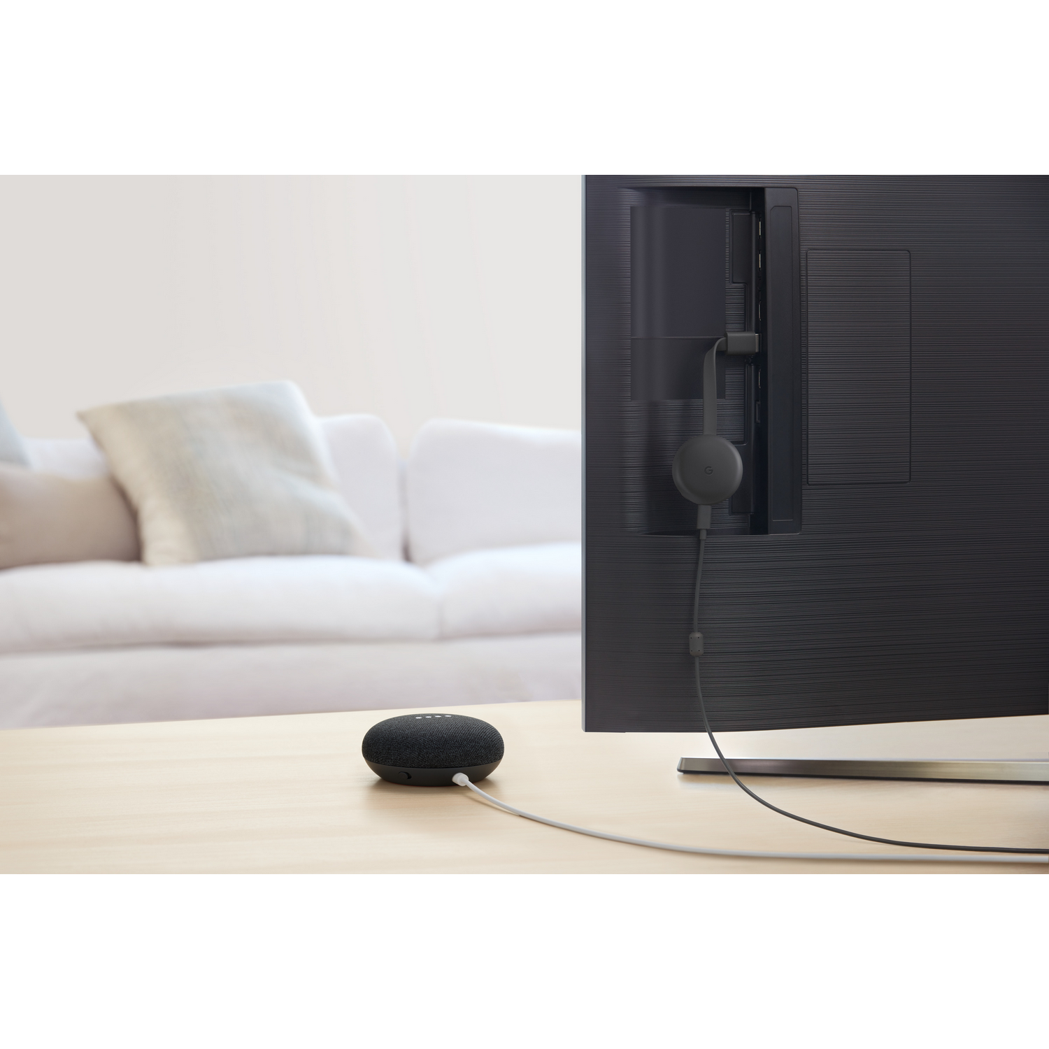 Un Google Home Mini negro en una mesa junto a un televisor con un Chromecast conectado.