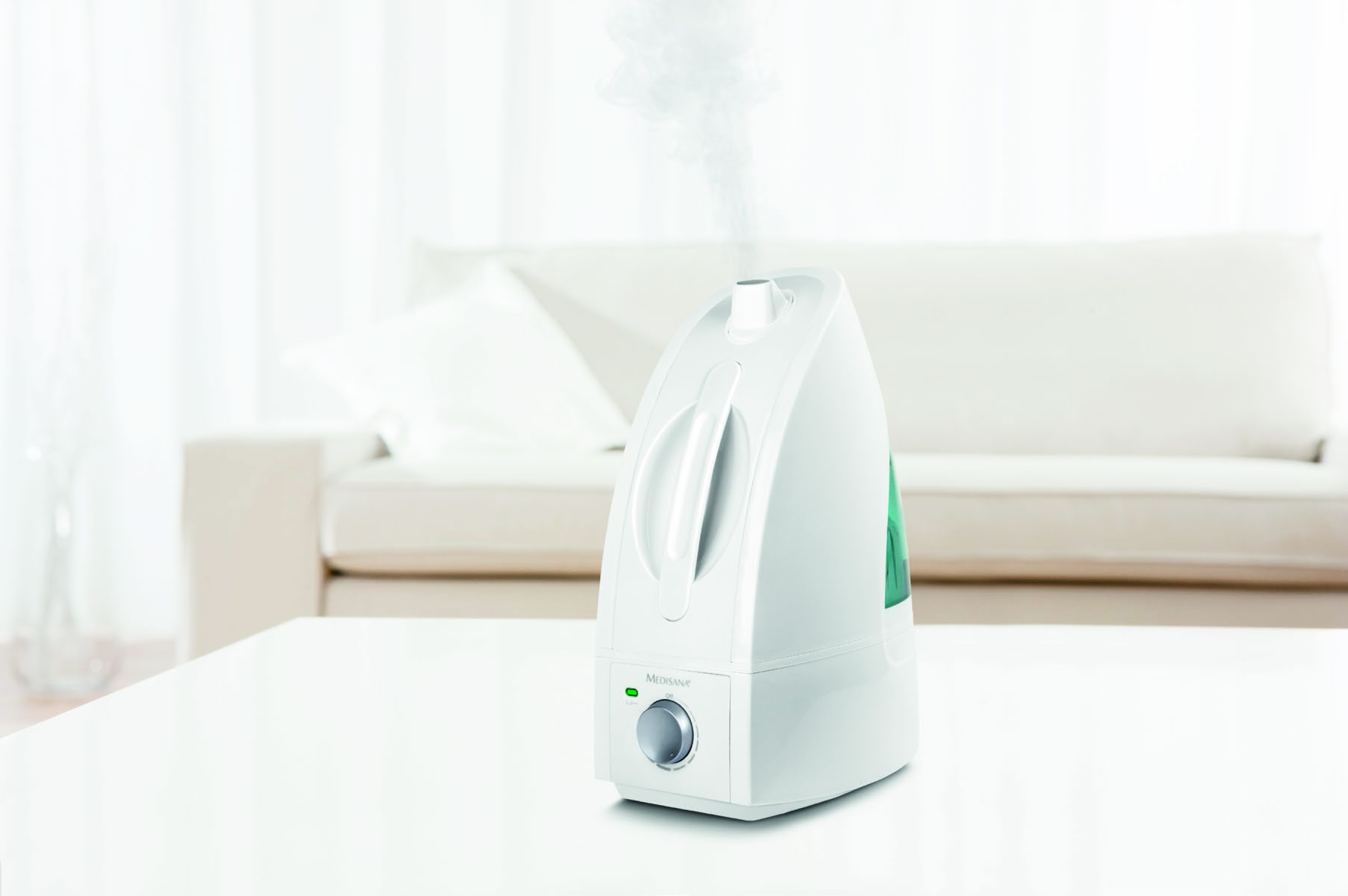 Un humidificateur blanc sur une table, de la vapeur sort. Un canapé est en arrière-plan.