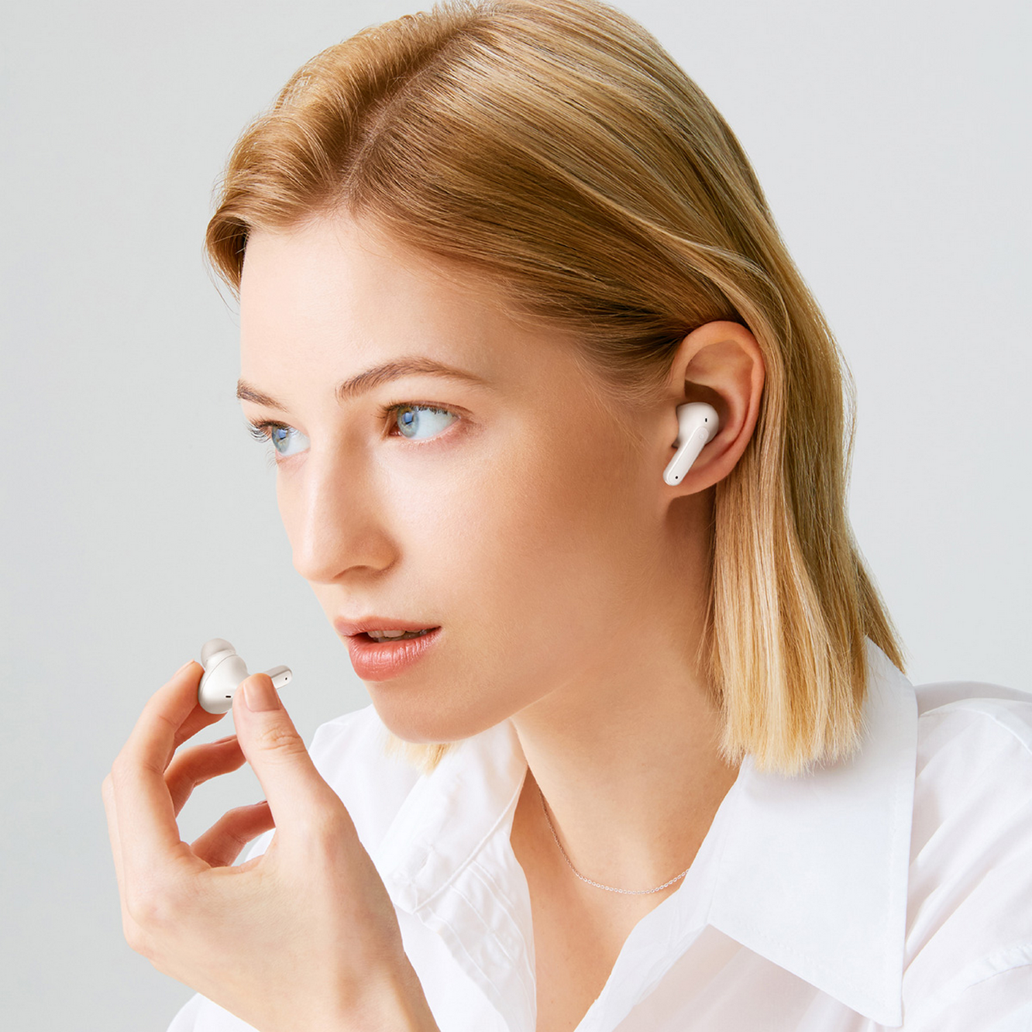 Mujer con auriculares blancos en las orejas. Sostiene otro auricular en la mano.