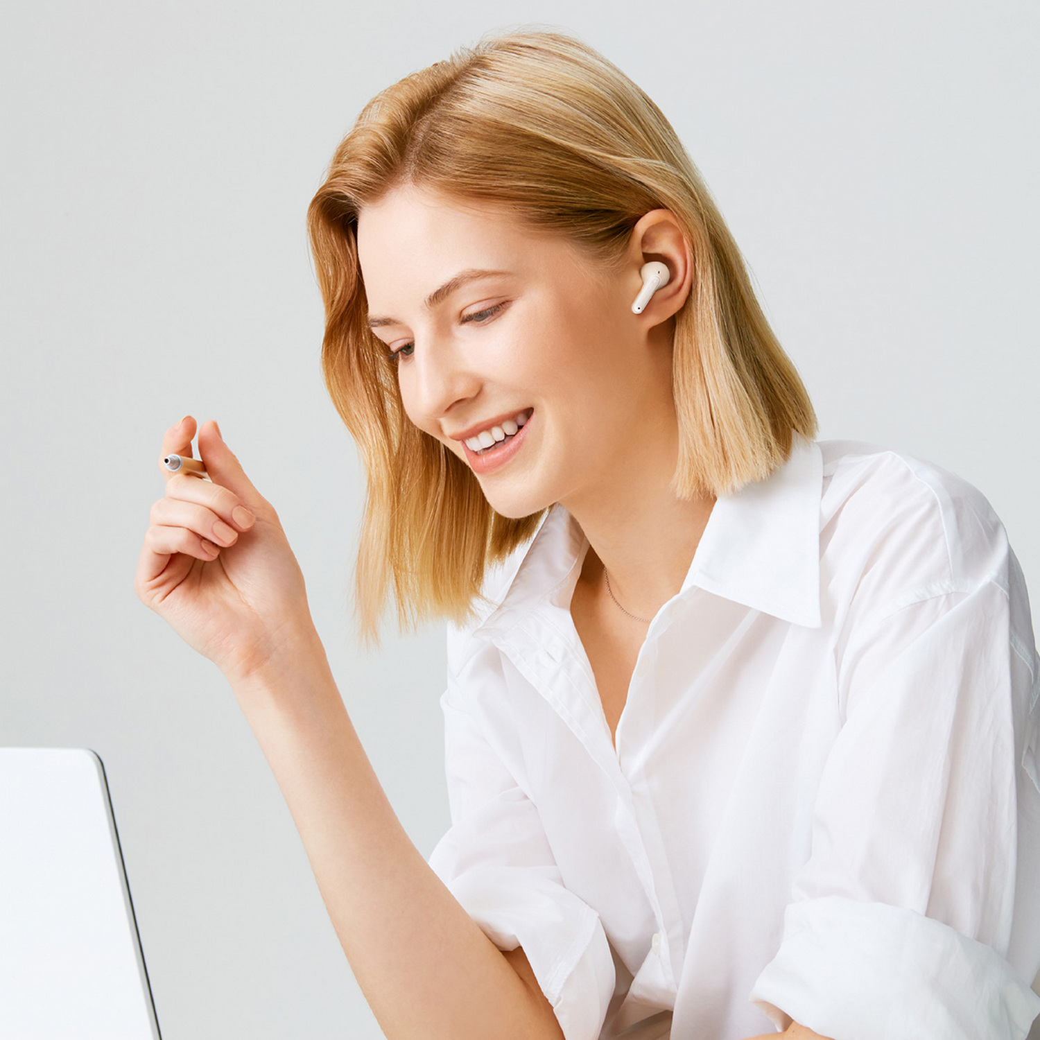 Mujer con auriculares, sonríe a una laptop. Pluma en mano. Camisa blanca.