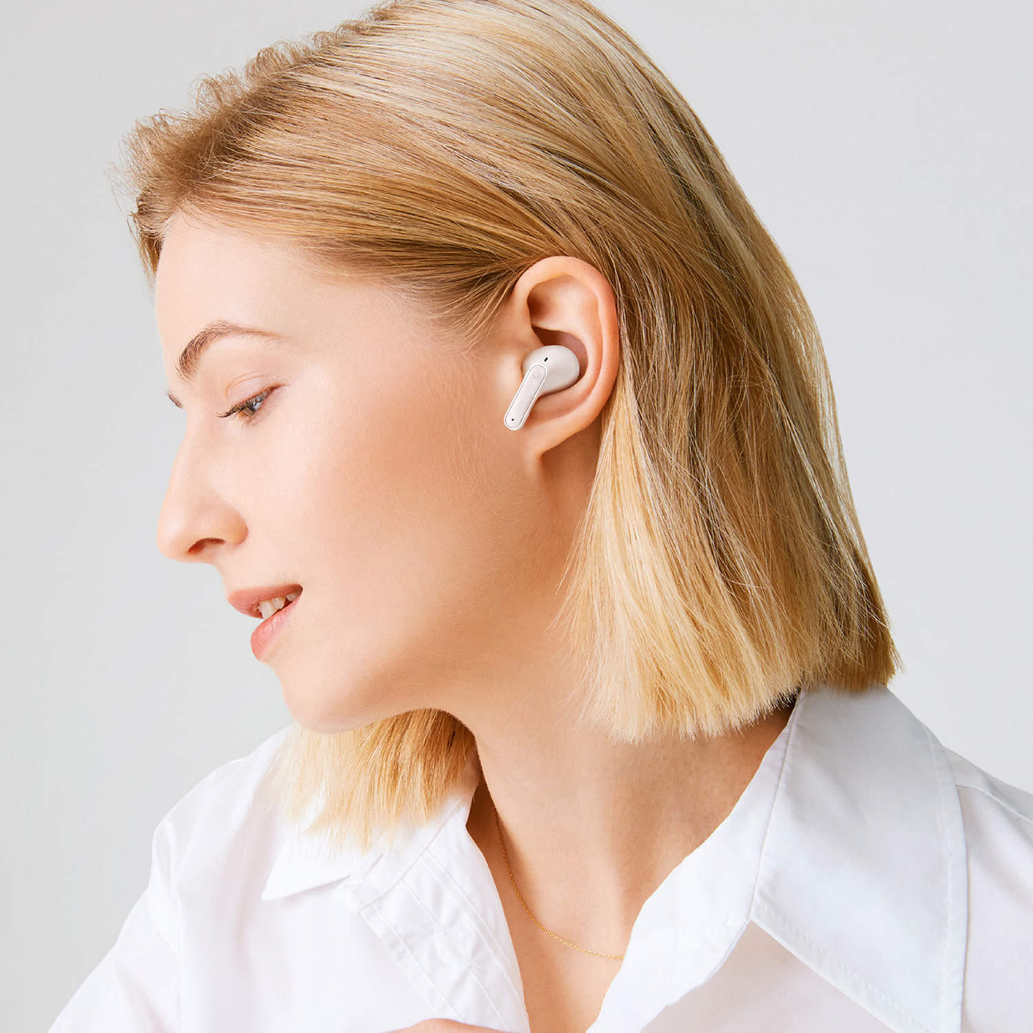 Una mujer con una camisa blanca escucha un auricular blanco en su oído.