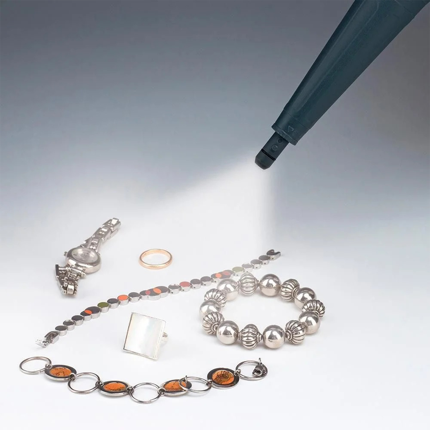 Una luce illumina gioielli: un orologio, anelli e bracciali, su sfondo bianco.